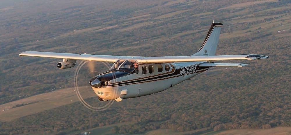 A white and red Cessna C210J Centurion flying over countryside